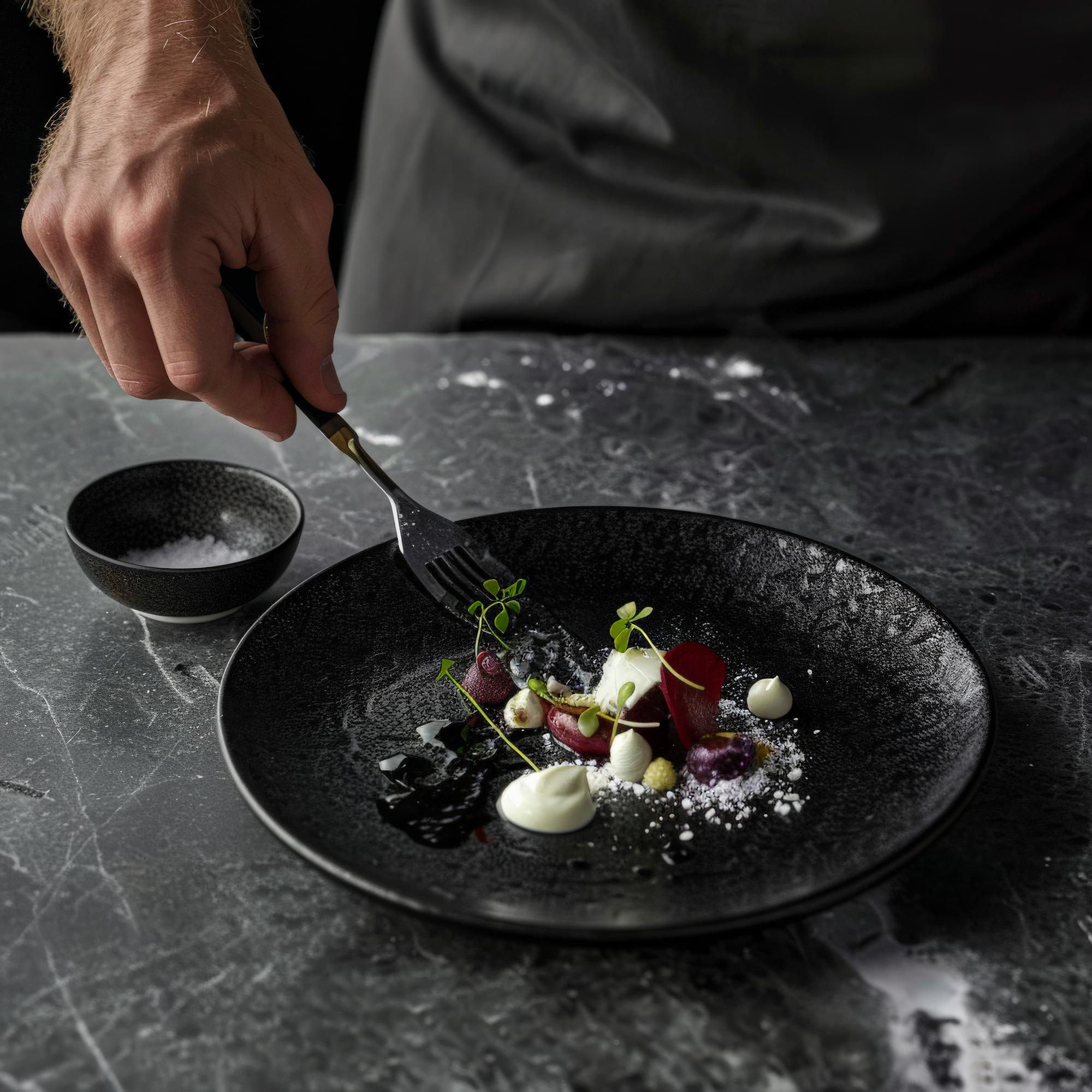 Chef preparing plated gourmet dish on dark table